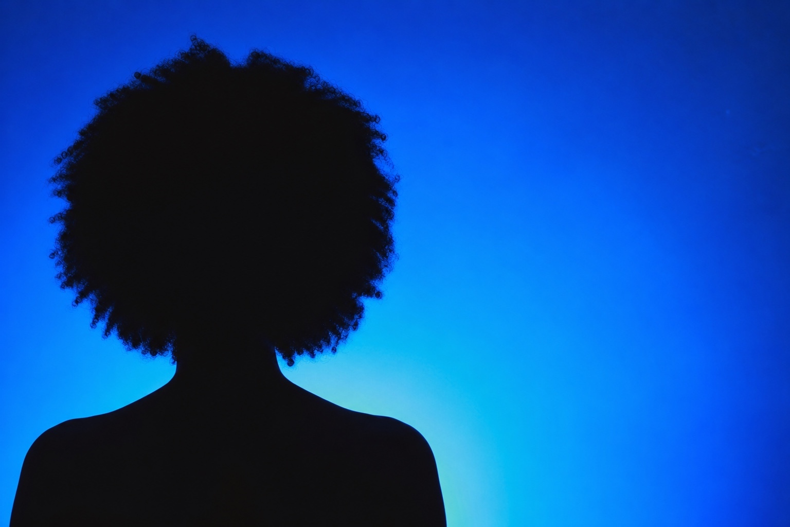 Back-facing silhouette of a woman with coily hair against a luminous blue background